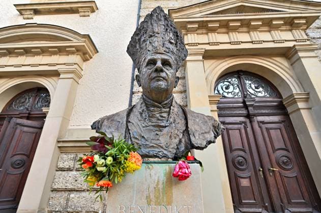 Pope Emeritus Benedict XVI has passed away Bust of Joseph Ratzinger as Pope Benedict XVI in front of the primatial church of St. Oswald in his Upper Bavarian hometown of Traunstein, with flowers and candles after the announcement of his death The bust is by Surberg artist Johann Brunner Traunstein Bavaria Germany Copyright: xRolfxPossx