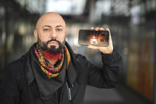 <p>Der Politiker Ferat Kocak (Die Linke) am 16. März 2022 am Berliner Bahnhof Südkreuz. Er zeigt auf seinem Handy ein Foto von seinem brennenden PKW der einem Anschlag zum Opfer fiel. Deutschland Berlin Copyright: RetoxKlar