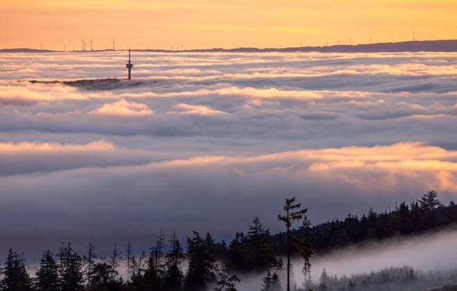 Sunrise over the fog View of the sunrise from the heights of the Taunus, valley is a thick blanket of fog to see, from which the highest peaks of the low mountain range stand out, in the center the summit of Winterstein Steinkopf In the background wind turbines of a wind farm , Schmitten Hesse Germany