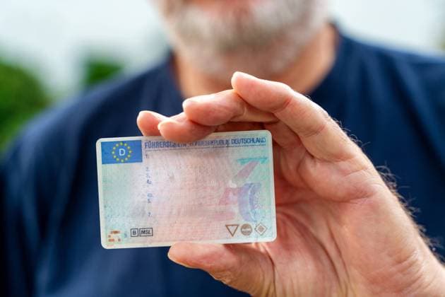 Augsburg, Bayern, Deutschland - 27 Oktober 2023: Ein alter Mann mit Bart hält einen Füherschein in der Hand. Fahrtauglichkeit im Alter Konzept FOTOMONTAGE