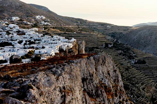 A scenic view of a traditional white village nestled in rugged hills, bathed in the warm glow of the setting sun. Folegandros Greece bola01007 Copyright: xConnectxImagesx