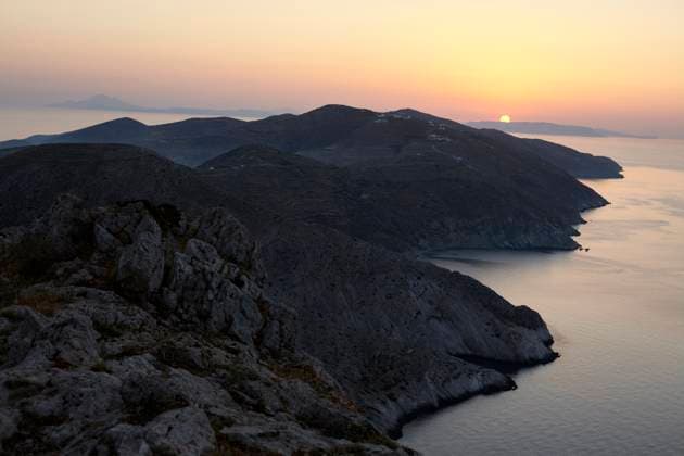 The sun sets behind a mountainous coastline, casting a warm glow over the serene seascape. Folegandros Greece bola01010 Copyright: xConnectxImagesx