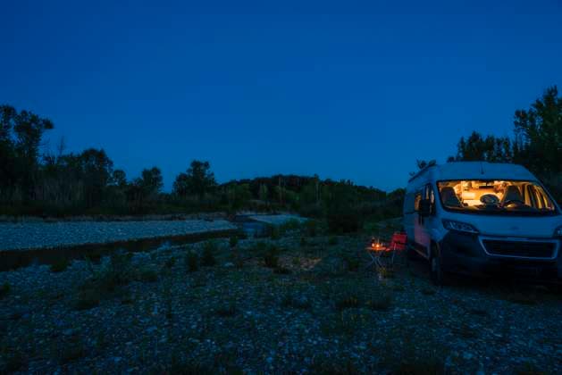 A man sits on a camping chair in front of a table on a blue hour summer evening in front of his campervan Germany On the road in a campervan