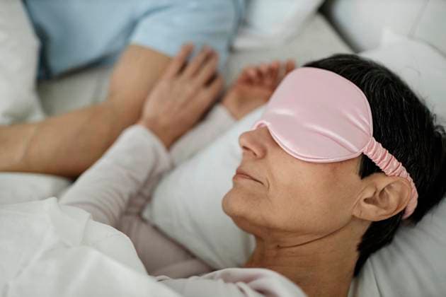 Woman wearing sleeping mask while lying in bed next to her husband model released, Symbolfoto, KPEF00336