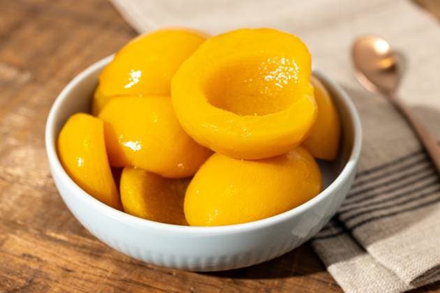 Nahaufnahme einer Schale mit Pfirsichhälften aus der Dose auf einem rustikalen Holztisch mit Serviette und Löffel Close up of a bowl full of canned peach halves on rustic wooden table with napkin and spoon Copyright: xZoonar.com AndresxVictorerox 22696392