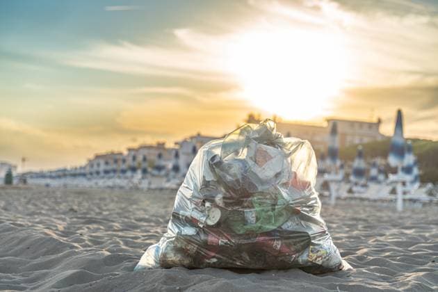 Italy - September 16, 2022: A filled garbage bag with plastic waste lies in the sand on a beach in Italy. The waste shows the environmental pollution and the problem of plastic waste in tourist coastal regions