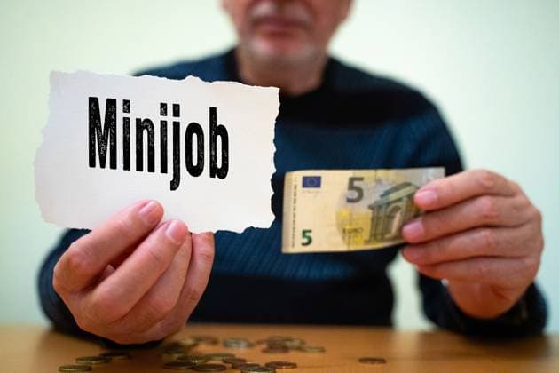 Munich, Bavaria, Germany - February 27, 2025: PHOTOMONTAGE. A man holds a sign saying Minijob and a 5-euro bill in his hand. Mini-jobs play an important role for low-income earners and pensioners who need to supplement their income.
