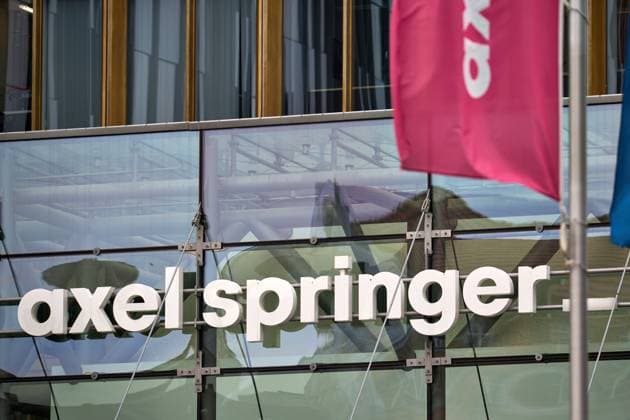 Berlin, Germany - March 27, 2025: Axel Springer lettering on the glass facade entrance of the publishing house in Berlin with reflected structures and waving company flags