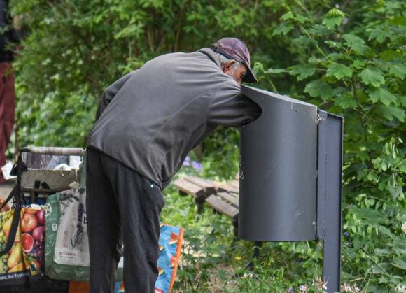 An elderly man searches a garbage can in a park in Berlin Friedrichshain for empty bottles