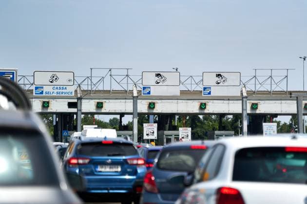 Autostrada, Italy - June 15, 2025: Vehicles wait in a queue and large crowds in front of a toll barrier with clearly visible symbols for cash and card payment. Green signals indicate open lanes.
