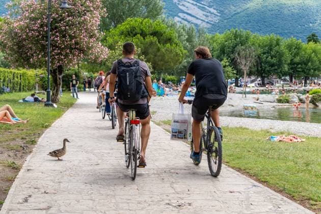 Nago-Torbole, Trentino, Italy - July 13, 2025: Holidaymakers cycle past bathing spots along the shore of Lake Garda near Torbole. The popular town is busy in summer, with tourists sharing cycle paths with walkers and animals