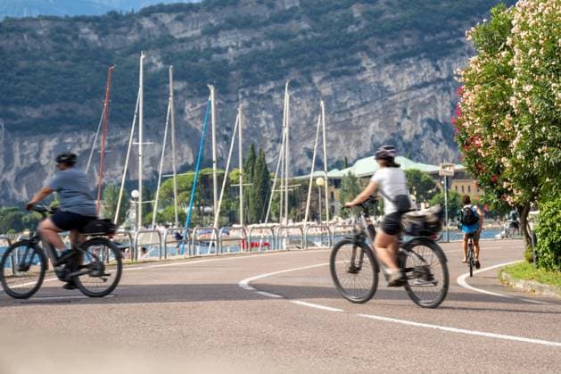 Torbole, Lake Garda, Italy - July 15, 2025: Cyclists on the promenade on Lake Garda - on the move with helmet and luggage along the lakeside road, where lake and mountains offer an active vacation route.