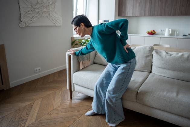 Ältere Frau, die sich wegen plötzlicher Wirbelsäulenschmerzen schmerzhaft an den Rücken klammert. Bandscheibenvorfall, Gelenkerkrankung Senior woman gripping lower back in severe pain from sudden spinal attack. Slipped disc, arthritic condition, muscle spasm, acute discomfort, standing difficulty, indoor scene, health emergency (License=RF) ,model released, Symbolfoto Copyright: xZoonar.com DmitriixMarchenkox 23824717 ,model released, Symbolfoto ,property released