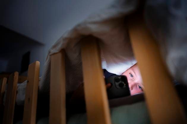 Symbolic photo Staged photo on the subject of media use by children A child looks at the display of a smartphone in the dark under the comforter in bed Berlin, 18 08 2025 Berlin Germany Copyright: xThomasxTrutschelx