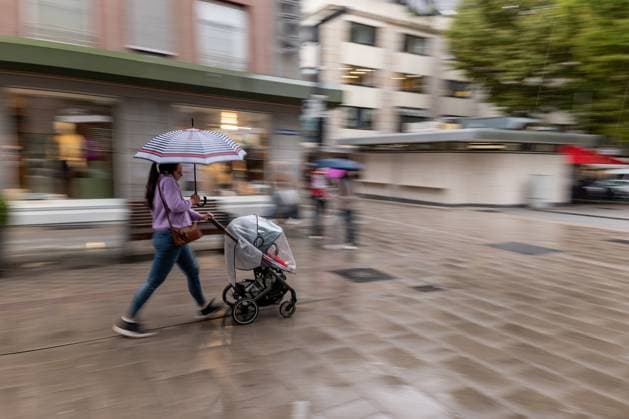 Woman with stroller in the rain 09 09 25, Limburg Symbol photo, illustration image, symbol image, illustration photo, everyday scene A woman pushes a stroller through a wet shopping street She holds a colorful umbrella and moves briskly while the surroundings blur in motion The picture shows an everyday scene in rainy weather in Copyright: xThorstenxWagnerx
