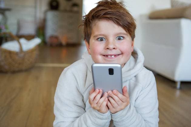 Germany - September 17, 2025: PHOTOMONTAGE, A child sits enthusiastically in the living room with a smartphone in their hand. The image shows digital media use in everyday life, entertainment, and the strong influence of technology on children. Digitally edited.