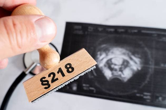 Bavaria, Germany - October 3, 2025: PHOTOMONTAGE, symbolic photo on the subject of abortion with wooden stamp Âß218 in front of an ultrasound image. Depiction of the legal and medical tensions surrounding abortion in Germany