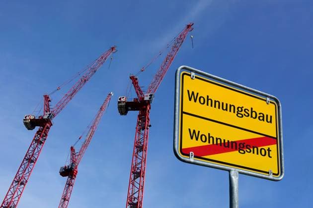 Construction cranes and town sign with the words Wohnungsbau and Wohnungsnot Photomontage Construction cranes and town sign with the words Wohnungsbau and Wohnungsnot, 13 10 2025, Next to several construction cranes is a town sign with the words Wohnungsbau and Wohnungsnot