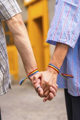 Männliches Paar, das seine Liebe und Unterstützung füreinander zeigt, indem es sich mit Regenbogenflaggen Armbändern an den Händen hält, die ihren lgbtq Plus Stolz und ihre Beziehung vor einem leuchtend gelben Hintergrund symbolisieren Male couple showing love and support for each other by holding hands with rainbow flag bracelets, symbolizing their lgbtq plus pride and relationship against a vibrant yellow background Copyright: imageBROKER UnaixHuizi ibxuhu15317625.jpg ,model released, Symbolfoto ,property released