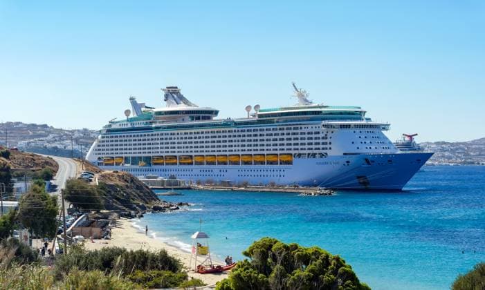 Mykonos, Cyclades, Greece Cruise ship Voyager of the Seas moored in Mykonos harbor Bay In front, tourists bathing on the sandy beach Paralia Agios Stefanos In the back, the old town of Mykonos Mykonos Mykonos Greece