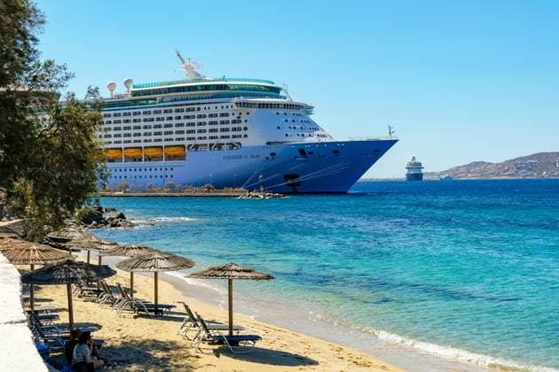 Mykonos, Cyclades, Greece Cruise ship Voyager of the Seas moored in Mykonos harbor bay Beach chairs and umbrellas in front on the sandy beach Paralia Agios Stefanos Mykonos Mykonos Greece