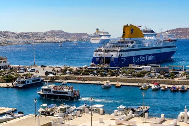 Mykonos, Cyclades, Greece Mykonos New Port, a ferry of the Blue Star Ferries lies at the quay in the new harbor in front of the skyline of Mykonos town In front a cab boat a sea bus brings the tourists to the old town In the back more cruise ships are moored in the bay in front of Mykonos town with a view of the old town with