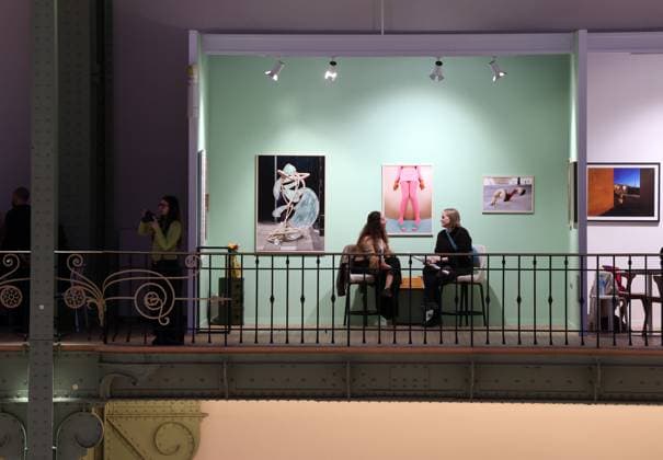 A visitor (R) to the Hama Gallery seats beneath photographs by Melissa Schriek on display of the 2025 Paris Photo Fair on the opening day at the Grand Palais, on Wednesday, November 12, 2025. The world s most important international photography fair brings together iconic and emerging names, showcasing 179 galleries from 33 countries and a rich programme that encompasses photography in all its forms, from silver gelatin to blockchain.  PAR20251112115 MAYAxVIDON-WHITE