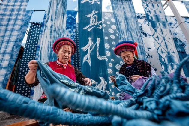 (251122) -- DALI, Nov. 22, 2025 -- Duan Yinmei (L), an inheritor of the tie-dye technique of Bai ethnic group, and handicraftsman Duan Lilan untie knots on fabrics in a dyehouse in Zhoucheng Village of Dali Bai Autonomous Prefecture, southwest China s Yunnan Province, Nov. 21, 2025. Known as the hometown of the tie-dye technique of Bai ethnic group, Zhoucheng Village hosts over 200 households engaging in tie-dye businesses, with the number of employees exceeding 4,000. As a traditional folk technique of the Bai ethnic group, tie-dye boasts a history spanning over a thousand years and was included in the first batch of China s national intangible cultural heritage list in 2006. Tying and dyeing are the core steps in the process of making