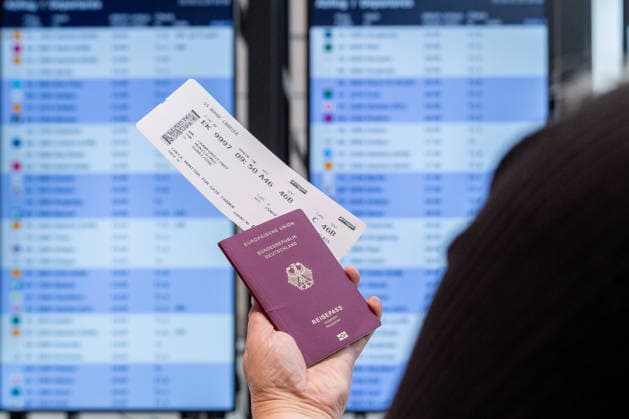 Bavaria, Germany - November 25, 2025: A traveler holds her flight ticket in front of the departure board at the airport. The scene shows typical procedures for air travel from checking flight information to preparing for boarding. On the day of trial operations for the new gate in Terminal 1 at Munich Airport.