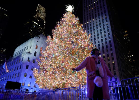 A reveler poses for a photograph with the Rockefeller Center Christmas Tree after it is lit for the first time of the season at the 93rd annual Rockefeller Center Christmas Tree lighting ceremony takes place in New York City on Wednesday, December 3, 2025. The 75-foot-tall Norway Spruce came from a home in East Greenbush, New York.  NYP20251203121 JOHNxANGELILLO