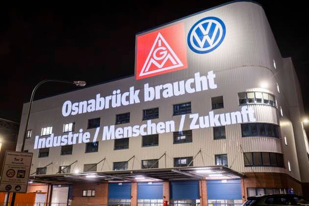 Projection of IG Metall logo and lettering Osnabrück needs industry people future next to the VW logo on the facade of the Osnabrück VW plant Peaceful protest rally of IG Metall in Osnabrück with on the situation automotive industry VW plant Osnabrück 08 12 2025 IG Metall rally in front of the VW plant Osnabrück