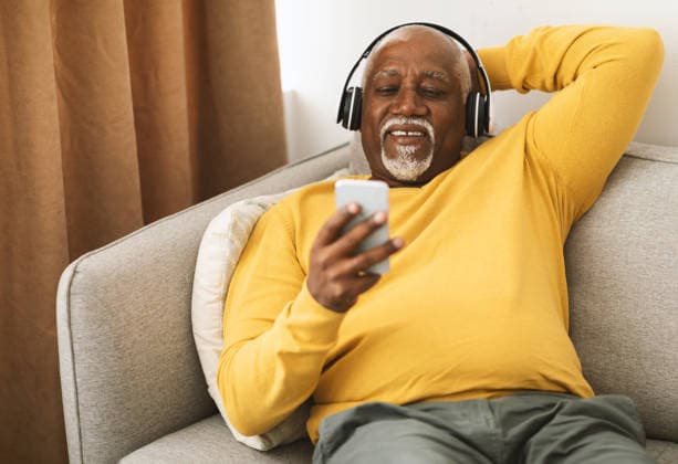 Senior African American Man Listening Music On Smartphone At Home Senior African American Man Listening To Music On Smartphone Sitting On Couch At Home. Male Wearing Headphones Enjoying Favorite Song Or Audiobook On Weekend. People And Gadgets, model released, , 97282328.jpg RECORD DATE NOT STATED