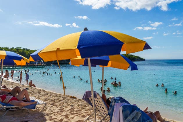 Isla Catalina, Dominican Republic, Caribbean - December 29, 2025: Vacationers lie in the shade under colorful parasols, while others swim in the clear sea and sunbathe. The scene depicts a typical summer vacation at the beach with relaxation, cooling off, and a sunny holiday atmosphere.