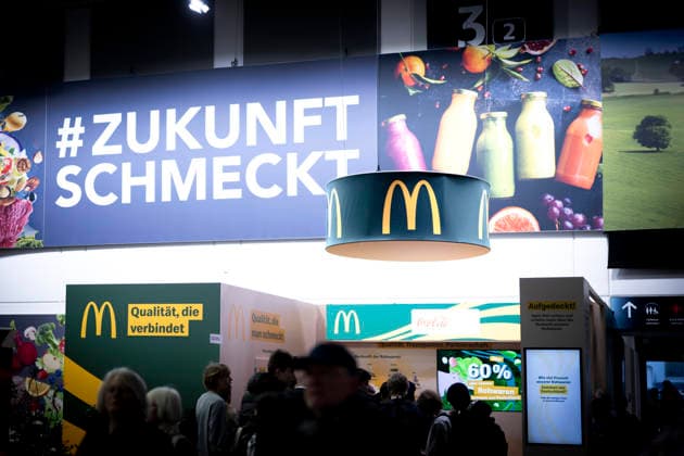 Gruene Woche Berlin DEU, Deutschland, Germany, Berlin, 23.01.2026 Besucher vor Logo Zukunft Schmeckt und Stand der fastfood Kette McDonald™s McDonald zum Thema Ernaehrungssicherheit und oekologische Landwirtschaft in der Biohalle vom Forum Moderne Landwirtschaft auf der Messe der Internationalen Gruenen Woche unter dem Motto Tradition trifft Zukunftsvisionen Gutes Essen Starkes Land Zukunftsfeste Landwirtschaft 100 Jahre 1926 - 2026 in Berlin Deutschland . Die Internationale Gruene Woche Berlin ist eine internationale Verbrauchermesse und Ausstellung der Ernaehrungswirtschaft Landwirtschaft Gartenbau und fuer landwirtschaftliche Produkte aus aller Welt. Die Messe gibt aktuellen gesellschaftlichen Fragen wie Klimaschutz Kreislaufwirtschaft