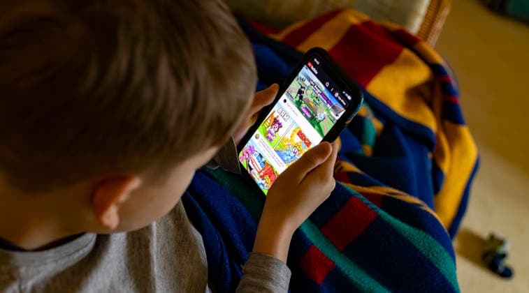 13 02 2026, Germany, an 8-year-old child watches the instructions for operating the online gaming platform Roblox on a cell phone via YouTube