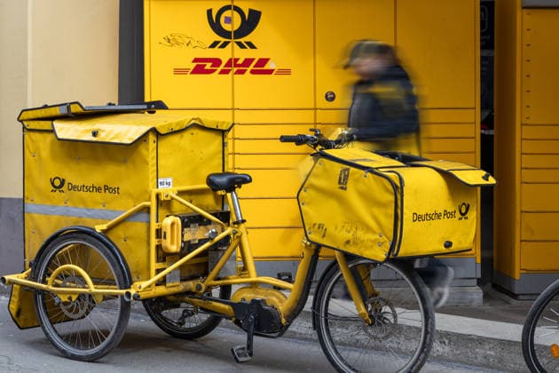 Augsburg, Bavaria, Germany March 19, 2026: A Deutsche Post delivery bike stands by while a mail carrier delivers and transports packages. The use of cargo bikes enables flexible and sustainable delivery in urban areas.