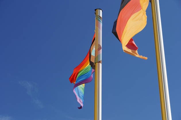 Progress Pride Flag, Progressive Rainbow flag and Flag the Federal Republic Germany to Two Flagpoles side by side, symbol for Diversity, Tolerance and the Representation from LGBTQIA On the right, queere People as Part the Company 1131608821