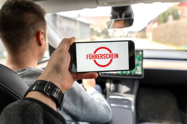 Bavaria, Allgäu, Germany April 5, 2026: A driver holds up a smartphone displaying the word driver™s license? and stands for changes in traffic law. The image symbolizes new rules, regulations, and adjustments related to driver™s licenses and traffic safety.