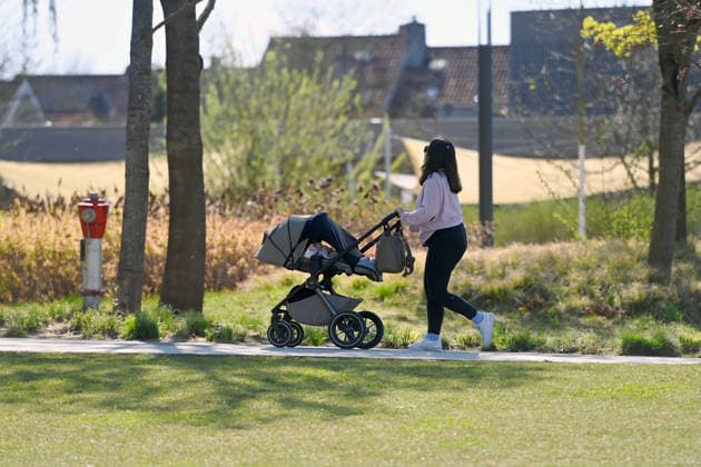 Woman pushing baby carriage through a park
