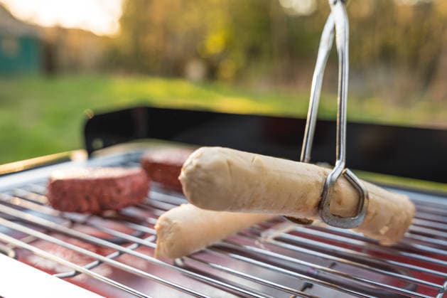 Bavaria, Germany April 7, 2026: During a springtime barbecue in the garden, tongs flip vegan sausages and plant-based steaks on the electric grill. Meat alternatives sit on the grill as an alternative to traditional barbecue fare