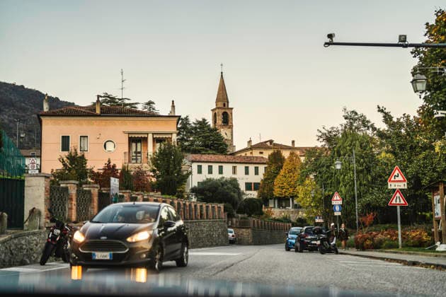 Vo, italy 28 october 2025: view of an italian village street at dusk, with an active moving car and a church bell tower rising above traditional buildings Italian village street at dusk with passing car Copyright: xx giro (245)