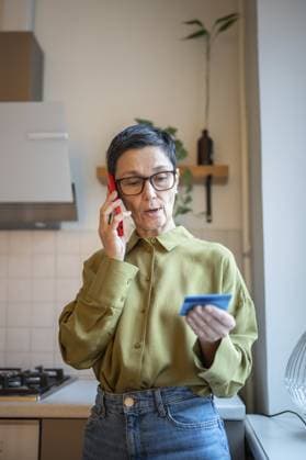 Besorgte ältere Frau, die auf ihrem Smartphone mit Betrügern spricht, eine Kreditkarte in der Hand hält und persönliche Daten an falsche Bankangestellte weitergibt. Verletzliche reife Frau, die von Finanzmanipulatoren telefonisch ausgetrickst wird Concerned elder woman talking on smartphone with scammers, holding credit card and sharing personal data to fake bank employees. Vulnerable mature female tricked by financial manipulators by phone Copyright: imageBROKER DmitriixMarchenko ibxiqx17289985.jpg ,model released, Symbolfoto ,property released