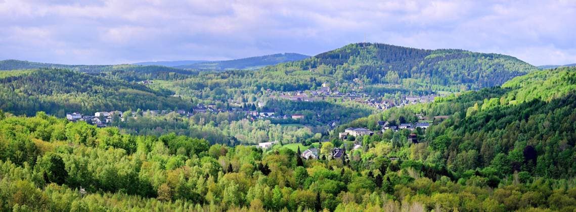 Neue Aussichtsplattform am Schacht 371 eröffnet Wismut macht Bergbaugeschichte erlebbar Blick über ein ehemaliges geschundenes Bergbaugelände der Wismut das sich heute als grüne Landschaft zeigt und 2027 die Landesgartenschau ausrichtet.Hier hat heute die Wismut GmbH am traditionsreichen Schacht 371 bei Hartenstein eine neue Aussichtsplattform eröffnet und damit einen weiteren öffentlich zugänglichen Ort geschaffen, an dem die Geschichte des Uranerzbergbaus im Westerzgebirge sichtbar und erfahrbar wird. Der Standort zählt zu den bedeutendsten Anlagen des ehemaligen SDAG Wismut Bergbaus. Der Schacht war bis zu seiner Stilllegung 1991 das tiefste Bergwerk Deutschlands. Die neue Plattform bietet einen freien Blick auf das weitläu Aue-Bad_SchlemaWismut-0605-26