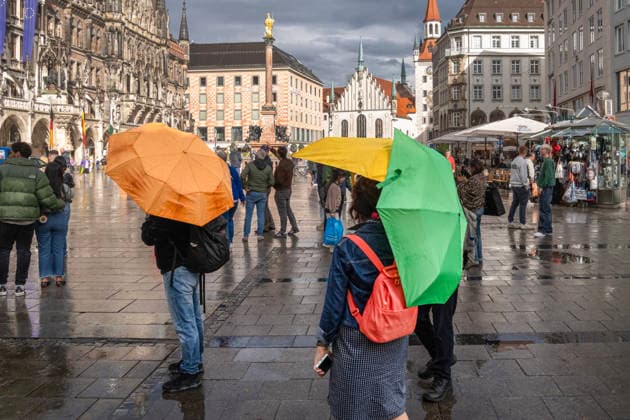 After a cloudburst and thunderstorm, the sun blinks through a gap in the clouds and bathes Marienplatz in a wonderful light, passers-by with colorful umbrellas, Munich, 6 May 2026 Germany, Munich, 6 May 2026, after a cloudburst the sun shines again over Marienplatz, passers-