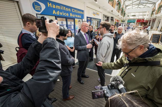 First Minister of Scotland John Swinney joins SNP candidate Alex Kerr campaigning in Hamilton - 06 May 2026 First Minister of Scotland John Swinney (centre) meets a voter in the constituency. The day before the Scottish parliamentary elections, First Minister of Scotland John Swinney visits Hamilton in South Lanarkshire, the constituency of SNP candidate Alex Kerr to kick off the final day of campaigning by meeting potential voters and owners of local businesses. Hamilton United Kingdom Copyright: xNeilxMiltonx xSOPAxImagesx L1000878