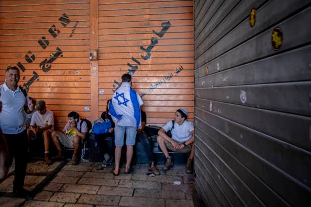 Jerusalem Day Flag Parade Israeli right wing youth draped in their national flag stands next to his friends sitting out side a closed Palestinian shop their in Damascus gate In Jerusalem, Thursday May 14 2026. Israeli nationalists, many of them teenagers and young adults, swept through the narrow streets of JerusalemÕs Old City on Thursday during the annual Jerusalem Day march, chanting ÒDeath to ArabsÓ and ÒMay your villages burnÓ as tens of thousands paraded to celebrate what Israeli authorities call the ÒreunificationÓ of Jerusalem following IsraelÕs capture and annexation of east Jerusalem in the 1967 Arab-Israeli war, while many Palestinian residents remained barricaded indoors and shopkeepers were forced, ostensibly for their own prot Copyright: xEyalxWarshavskyx