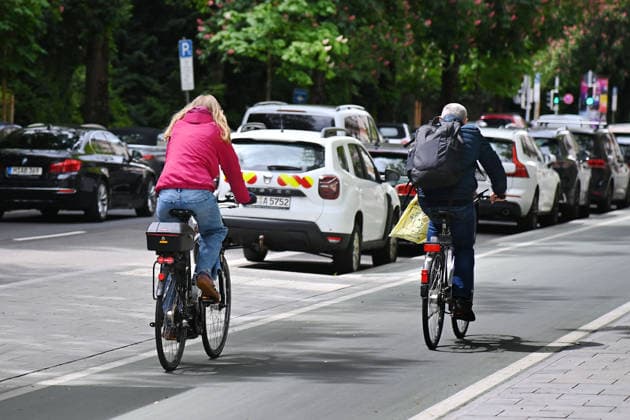 Cyclists ride on a wide cycle path, fast cycle path in Munich in city traffic, cycling, parked cars, cars, parking