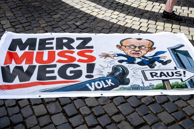 Augsburg, Bavaria, Germany May 16, 2026: Demonstration in Augsburg against the current federal government led by Chancellor Friedrich Merz. Under the slogan: Merz must go! Banner with the inscription: MERZ MUST GO! Featuring an illustration of a foot standing on the word PEOPLE and an illustration of Chancellor Friedrich Merz (CDU) flying through a door with a sign reading: GET OUT!