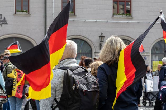 Augsburg, Bavaria, Germany May 16, 2026: Demonstration in Augsburg against the current federal government led by Chancellor Friedrich Merz. The slogan: Merz must go! Several demonstrators carry and wave German flags during the rally in downtown Augsburg