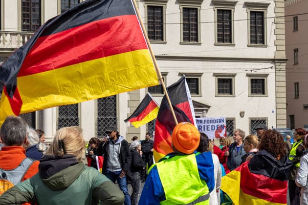 Augsburg, Bavaria, Germany May 16, 2026: Demonstration in Augsburg against the current federal government led by Chancellor Friedrich Merz. The slogan: Merz must go! Several demonstrators carry and wave German flags during the rally in downtown Augsburg